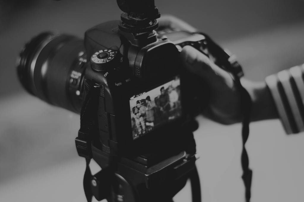 Gros plan en noir et blanc d'un appareil photo reflex professionnel monté sur un trépied, dont l'écran LCD affiche une image en cours de cadrage, tenu par la main d'un photographe.